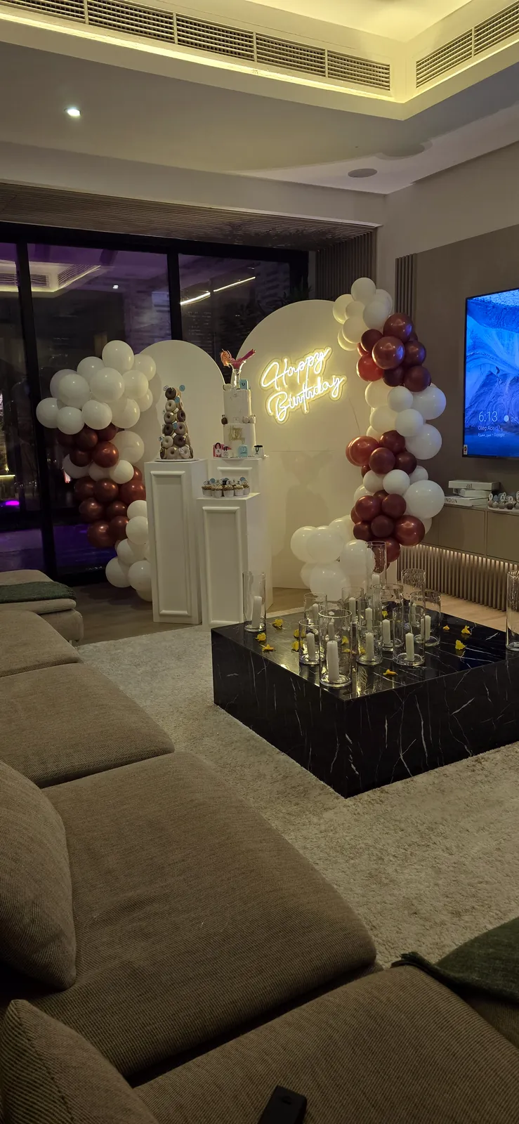 White and burgundy balloon arch with display stands in a living room with sofas