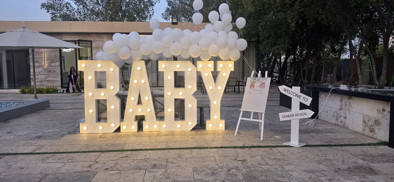 حروف مضيئة تكتب BABY تحت سحابة من البالونات البيضاء على تراس