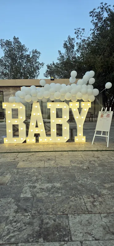 Светящиеся буквы BABY с белыми шарами на каменной террасе в сумерках